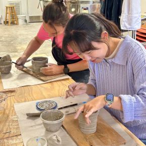 Two women in a clay studio building mugs out of clay using the coil building method.