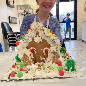 Girl with giant and highly decorated gingerbread house in front of her