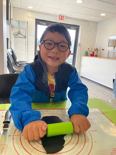 a boy with a green rolling pin rolling out black fondant